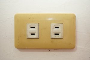 An old two-prong electrical outlet showing signs of aging and discoloration in a pre-1980 Los Angeles home.